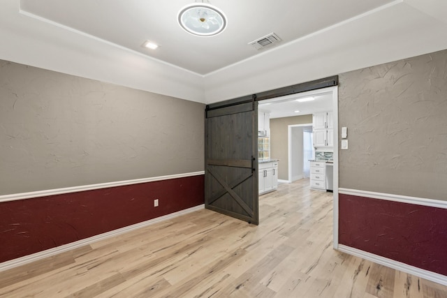 unfurnished room with a barn door and light hardwood / wood-style floors