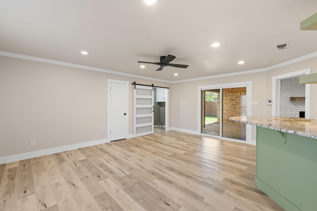 unfurnished living room with light wood-type flooring, a barn door, ceiling fan, and ornamental molding