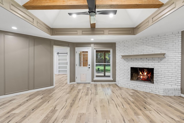 unfurnished living room featuring beam ceiling, ceiling fan, a fireplace, and light hardwood / wood-style flooring