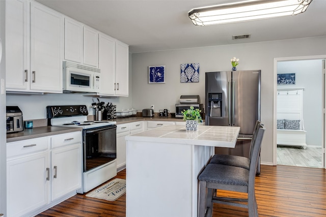 kitchen with white appliances, dark wood-type flooring, a breakfast bar, white cabinetry, and a kitchen island