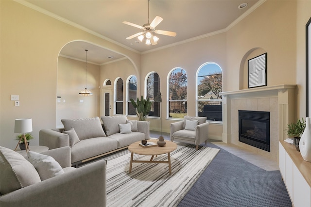 living room featuring ceiling fan, a tiled fireplace, light colored carpet, a high ceiling, and ornamental molding