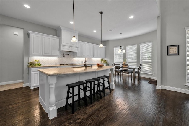 kitchen with sink, an island with sink, pendant lighting, decorative backsplash, and white cabinets