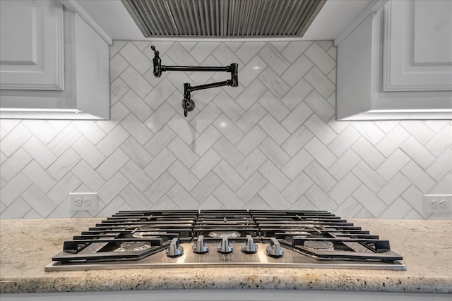 interior space featuring light stone counters, tasteful backsplash, stainless steel gas cooktop, and white cabinets