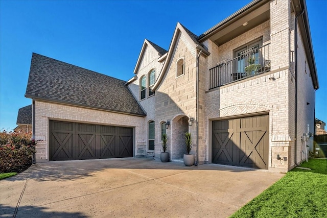 view of front of house featuring driveway, a shingled roof, a balcony, an attached garage, and brick siding