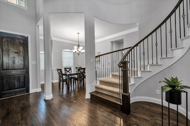 foyer entrance featuring a notable chandelier, crown molding, a wealth of natural light, and dark wood-type flooring