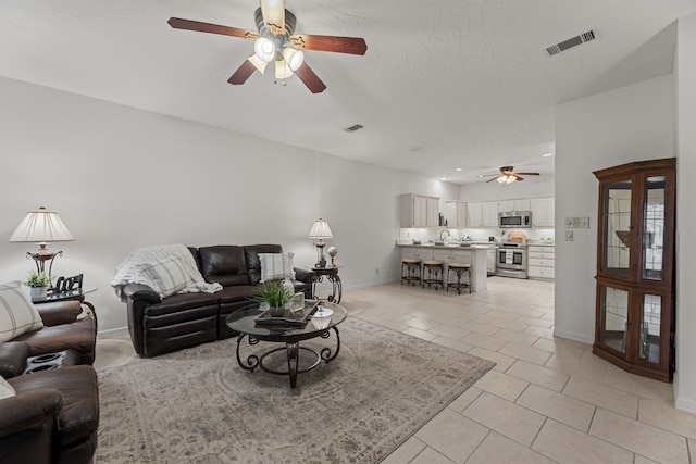 living room featuring a textured ceiling, ceiling fan, light tile patterned flooring, and sink