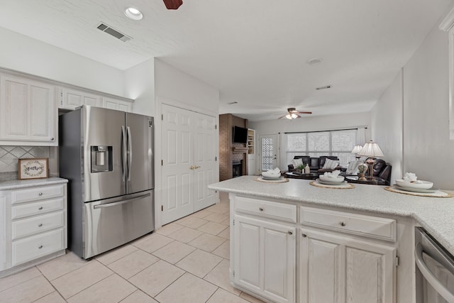 kitchen with white cabinets, ceiling fan, stainless steel appliances, and a brick fireplace