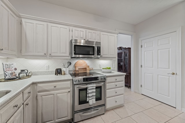 kitchen with white cabinets, light tile patterned floors, stainless steel appliances, and decorative backsplash