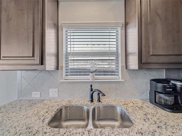 kitchen with backsplash, light stone counters, dark brown cabinetry, and sink