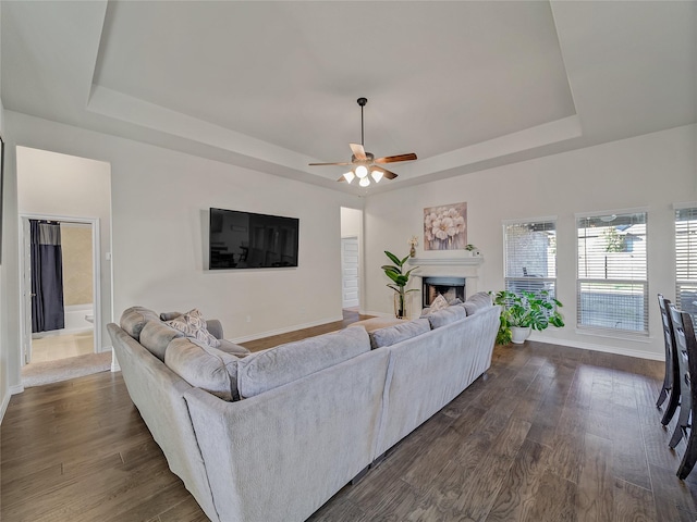 living room with ceiling fan, dark hardwood / wood-style flooring, and a tray ceiling