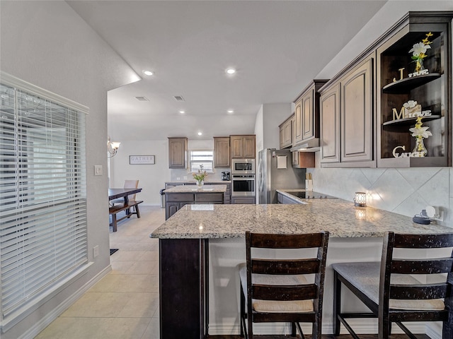 kitchen with kitchen peninsula, backsplash, a breakfast bar, stainless steel appliances, and light tile patterned floors