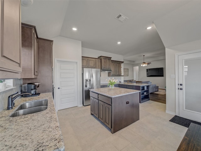 kitchen featuring sink, ceiling fan, stainless steel fridge, a kitchen island, and light stone counters