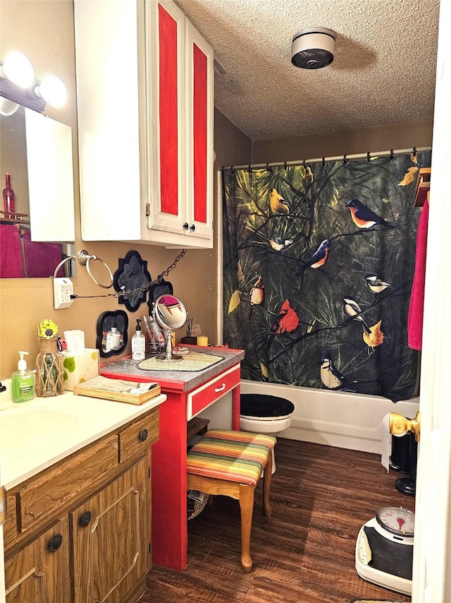 full bathroom with hardwood / wood-style floors, vanity, toilet, shower / bath combo with shower curtain, and a textured ceiling