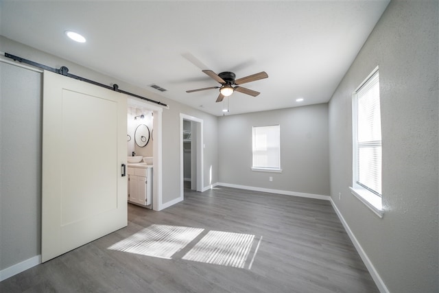 unfurnished bedroom with ceiling fan, a barn door, hardwood / wood-style floors, connected bathroom, and a closet