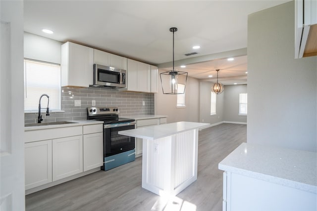 kitchen with white cabinets, hanging light fixtures, decorative backsplash, appliances with stainless steel finishes, and a kitchen island