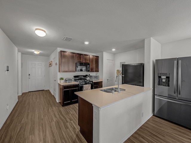 kitchen featuring dark brown cabinetry, a kitchen island with sink, sink, black appliances, and hardwood / wood-style flooring