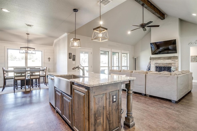 kitchen with light stone counters, decorative light fixtures, dishwasher, a fireplace, and an island with sink