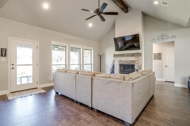 living room featuring dark hardwood / wood-style flooring, ceiling fan, lofted ceiling with beams, a stone fireplace, and plenty of natural light