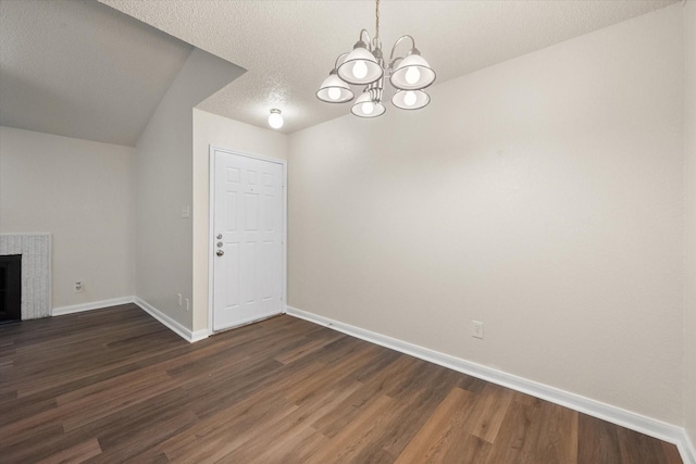 unfurnished dining area with a textured ceiling, dark hardwood / wood-style floors, an inviting chandelier, and a tiled fireplace