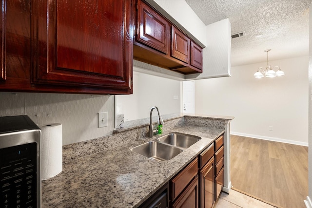 kitchen with an inviting chandelier, sink, a textured ceiling, decorative light fixtures, and light stone counters