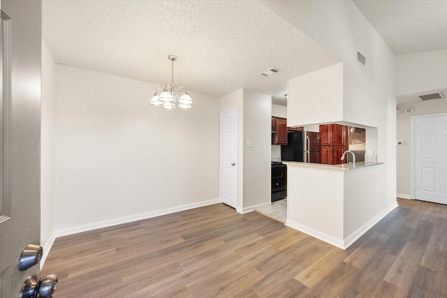 kitchen with range with electric cooktop, an inviting chandelier, kitchen peninsula, stainless steel fridge, and wood-type flooring