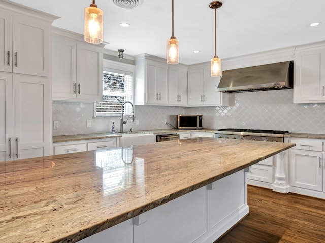 kitchen with decorative light fixtures, white cabinetry, and wall chimney range hood