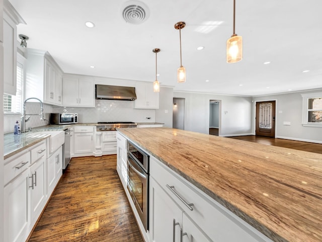 kitchen featuring wall chimney exhaust hood, stainless steel appliances, light stone counters, decorative light fixtures, and white cabinets