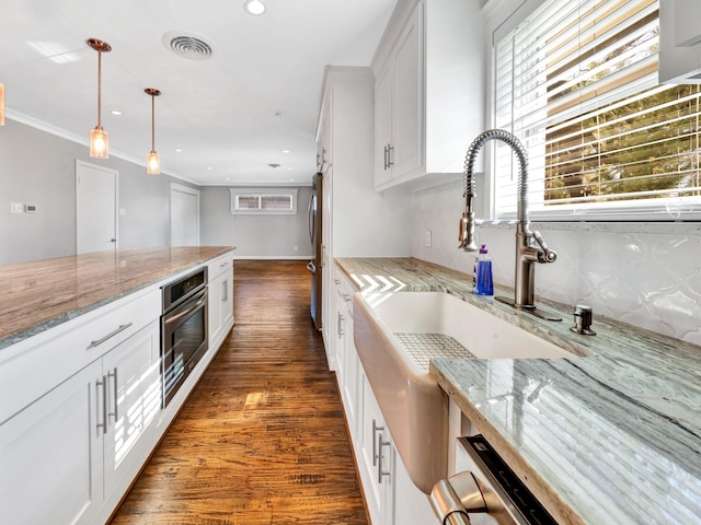 kitchen with appliances with stainless steel finishes, dark hardwood / wood-style flooring, light stone counters, pendant lighting, and white cabinetry