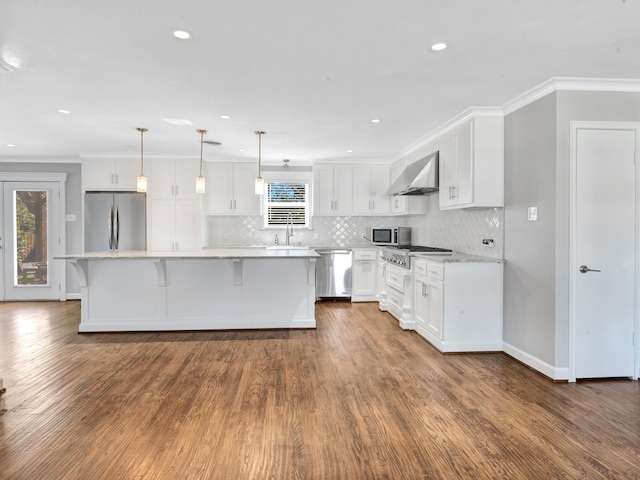 kitchen featuring a center island, wall chimney exhaust hood, crown molding, decorative light fixtures, and appliances with stainless steel finishes