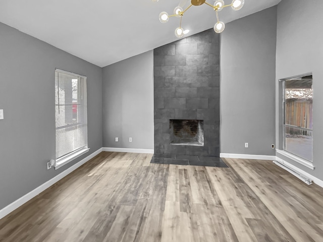 unfurnished living room with hardwood / wood-style floors, an inviting chandelier, a tile fireplace, and lofted ceiling