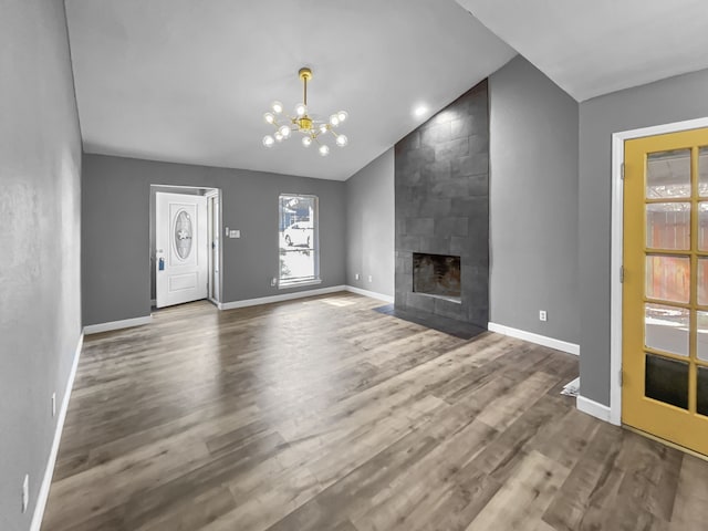 unfurnished living room with an inviting chandelier, a tile fireplace, vaulted ceiling, and wood-type flooring