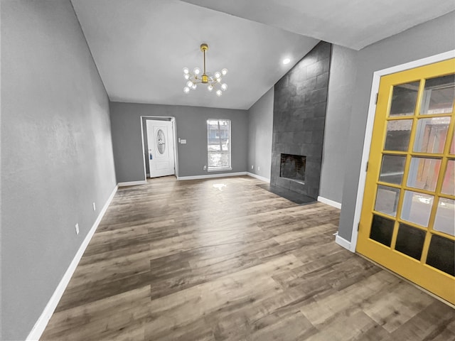 unfurnished living room with a tile fireplace, wood-type flooring, vaulted ceiling, and a chandelier