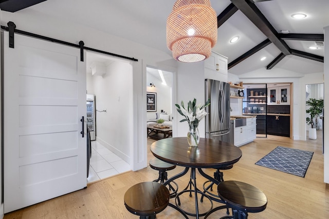 dining space with a barn door, light hardwood / wood-style flooring, and vaulted ceiling with beams