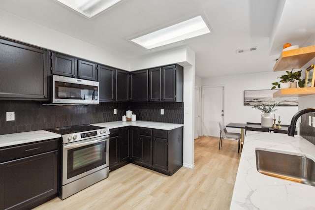 kitchen with sink, light stone countertops, appliances with stainless steel finishes, tasteful backsplash, and light hardwood / wood-style floors