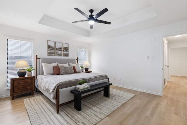 bedroom with a tray ceiling, multiple windows, ceiling fan, and light hardwood / wood-style floors