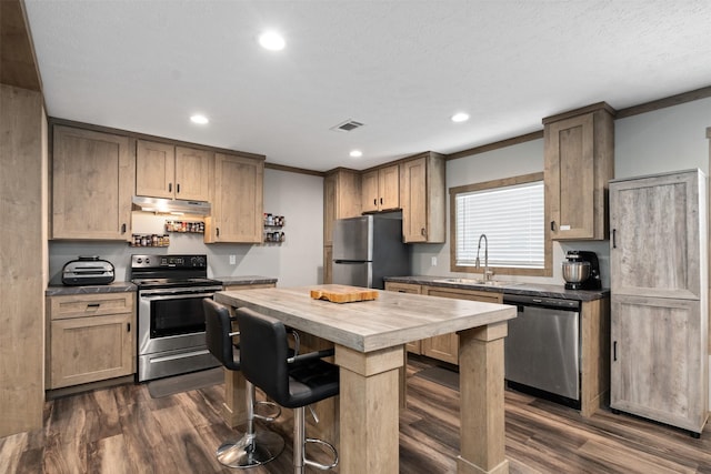 kitchen with appliances with stainless steel finishes, ornamental molding, a breakfast bar, sink, and a center island