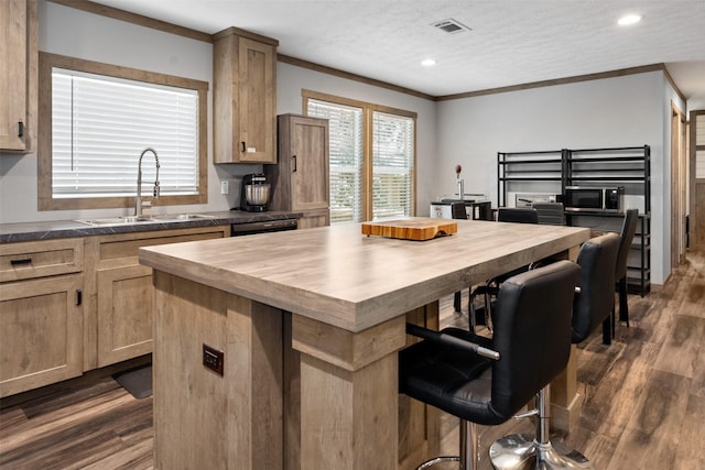 kitchen featuring sink, ornamental molding, a textured ceiling, a kitchen island, and dark hardwood / wood-style flooring