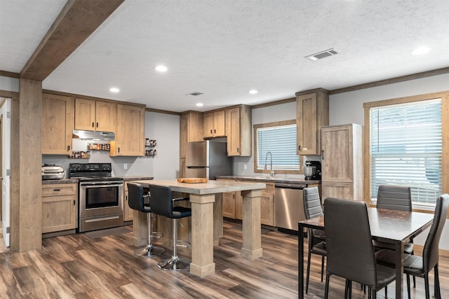 kitchen with dark wood-type flooring, crown molding, a textured ceiling, a kitchen island, and appliances with stainless steel finishes