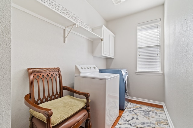 clothes washing area featuring cabinets, light wood-type flooring, washer and dryer, and a healthy amount of sunlight