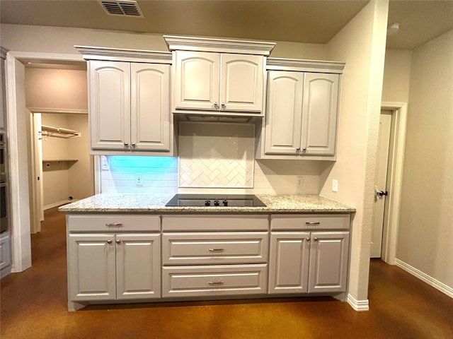 kitchen featuring black electric stovetop, oven, light stone counters, and backsplash