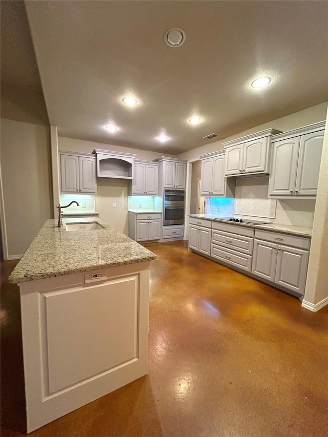 kitchen featuring light stone countertops, sink, stainless steel double oven, backsplash, and black electric cooktop