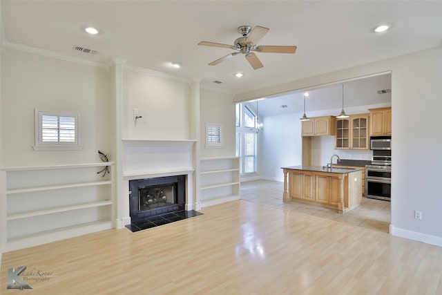 kitchen with light wood-type flooring, stainless steel appliances, ceiling fan, a tile fireplace, and decorative light fixtures