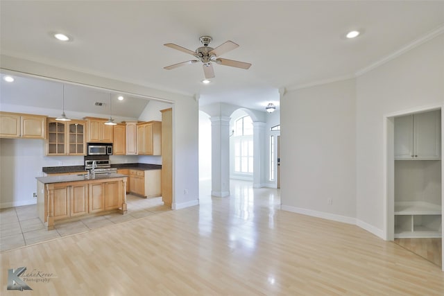 kitchen featuring ornate columns, ornamental molding, light hardwood / wood-style floors, hanging light fixtures, and an island with sink