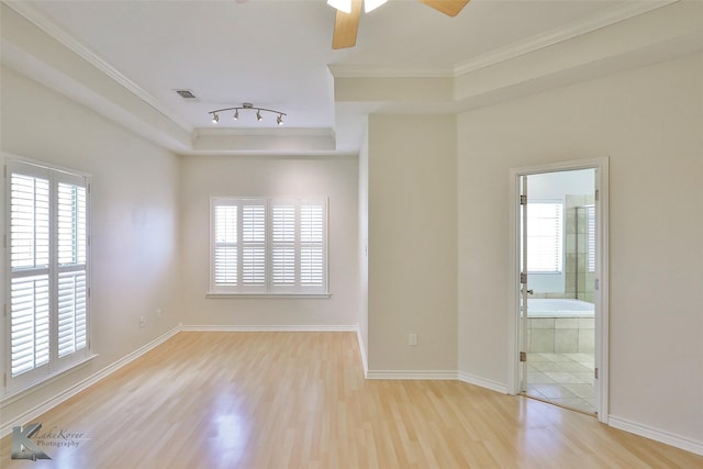 empty room with a raised ceiling, ceiling fan, light wood-type flooring, and ornamental molding