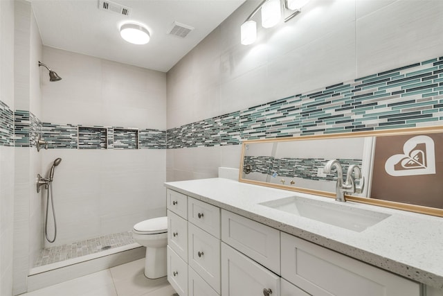 bathroom featuring vanity, tiled shower, tile walls, tile patterned flooring, and toilet