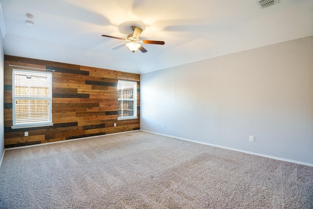 carpeted empty room featuring ceiling fan, a wealth of natural light, and wood walls