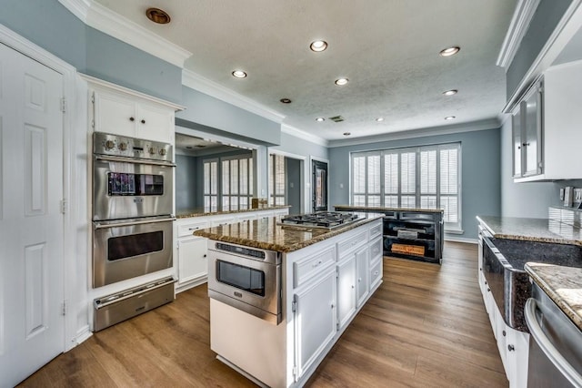 kitchen with dark stone counters, stainless steel appliances, white cabinets, hardwood / wood-style floors, and a center island