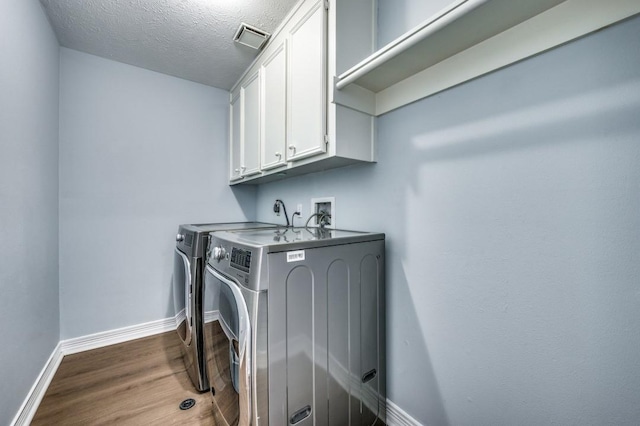 washroom with cabinets, washer and dryer, a textured ceiling, and hardwood / wood-style flooring