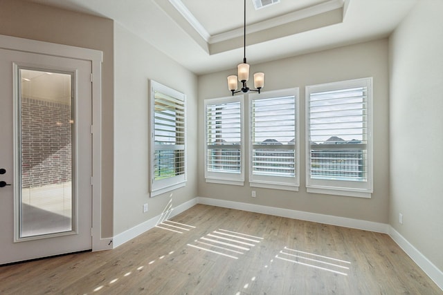 unfurnished dining area featuring a chandelier, light hardwood / wood-style floors, a raised ceiling, and crown molding