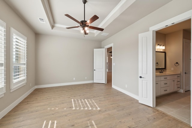 unfurnished bedroom with a raised ceiling, sink, ensuite bath, ceiling fan, and light wood-type flooring